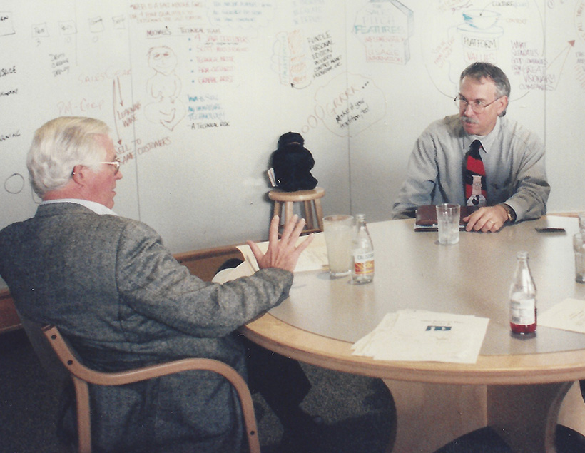 Two men sitting at a table talking to each other.