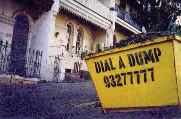 A yellow dumpster sitting in front of a white house.